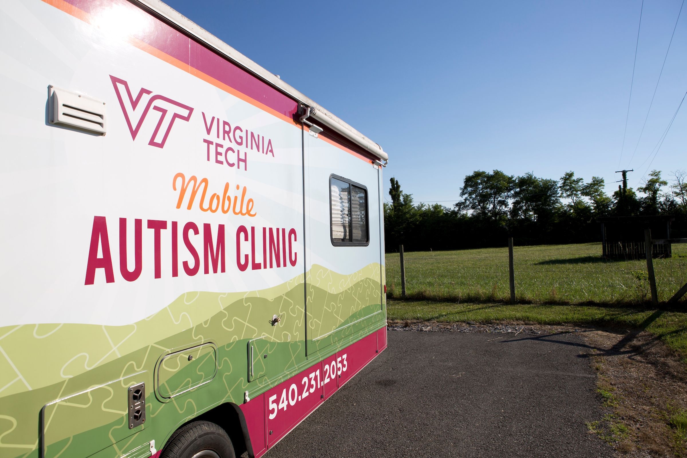 Drivers side of parked RV with logo VT Mobile Autism Clinic and fence off to the right in background